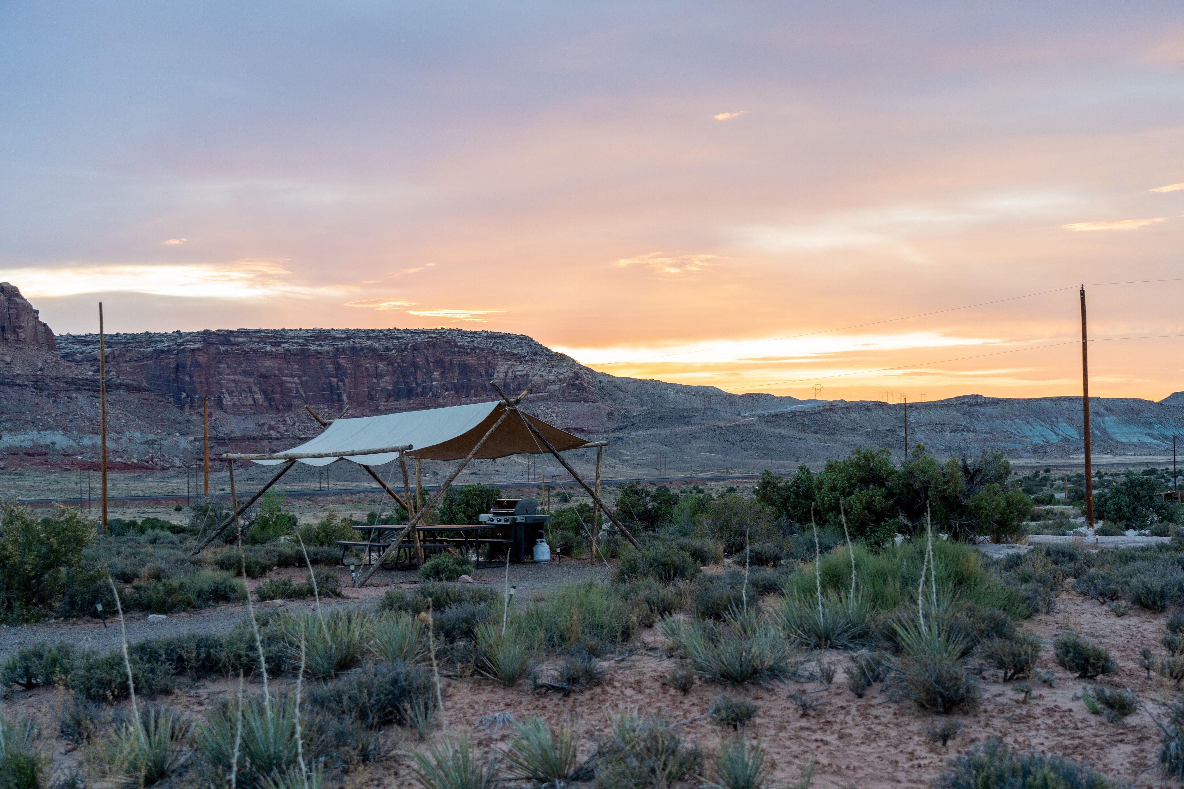A desert campsite with a tent, a table, and a grill.
