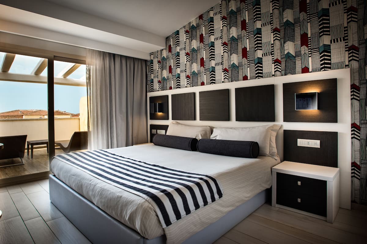 A modern hotel room with a large bed, a balcony with a view, and a patterned wall.
