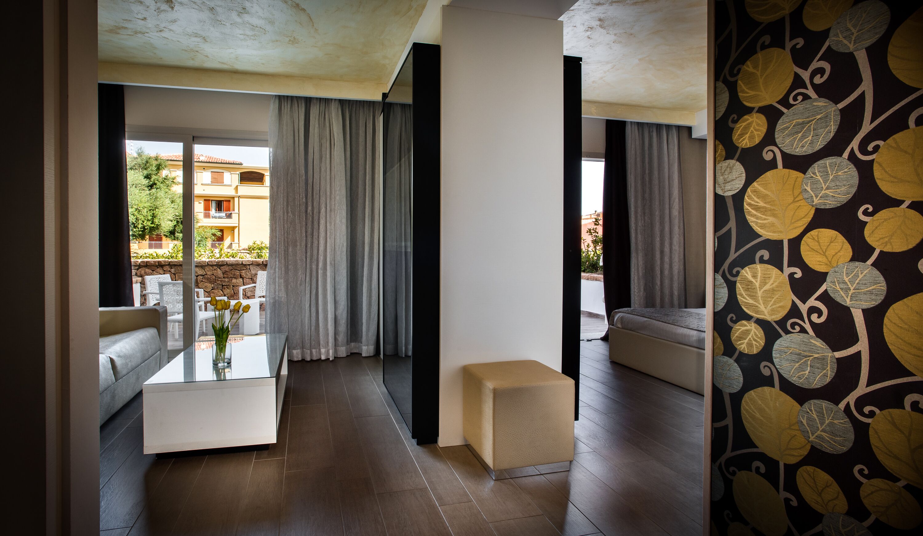 Un salon moderne avec une table basse en verre, un canapé beige et une grande fenêtre avec des rideaux.