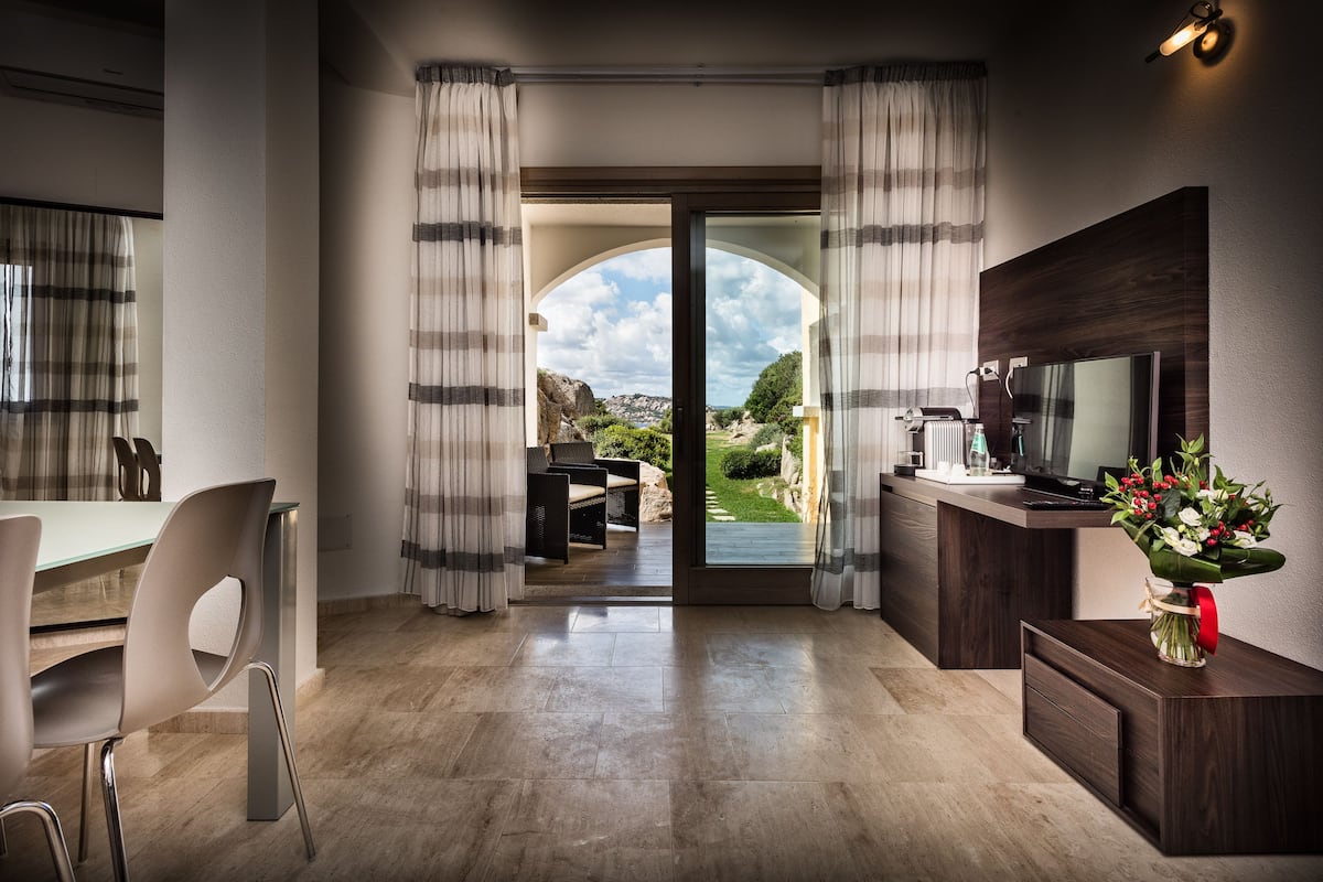 A modern interior with a dining area, a TV, and a view through a glass door to an outdoor garden.