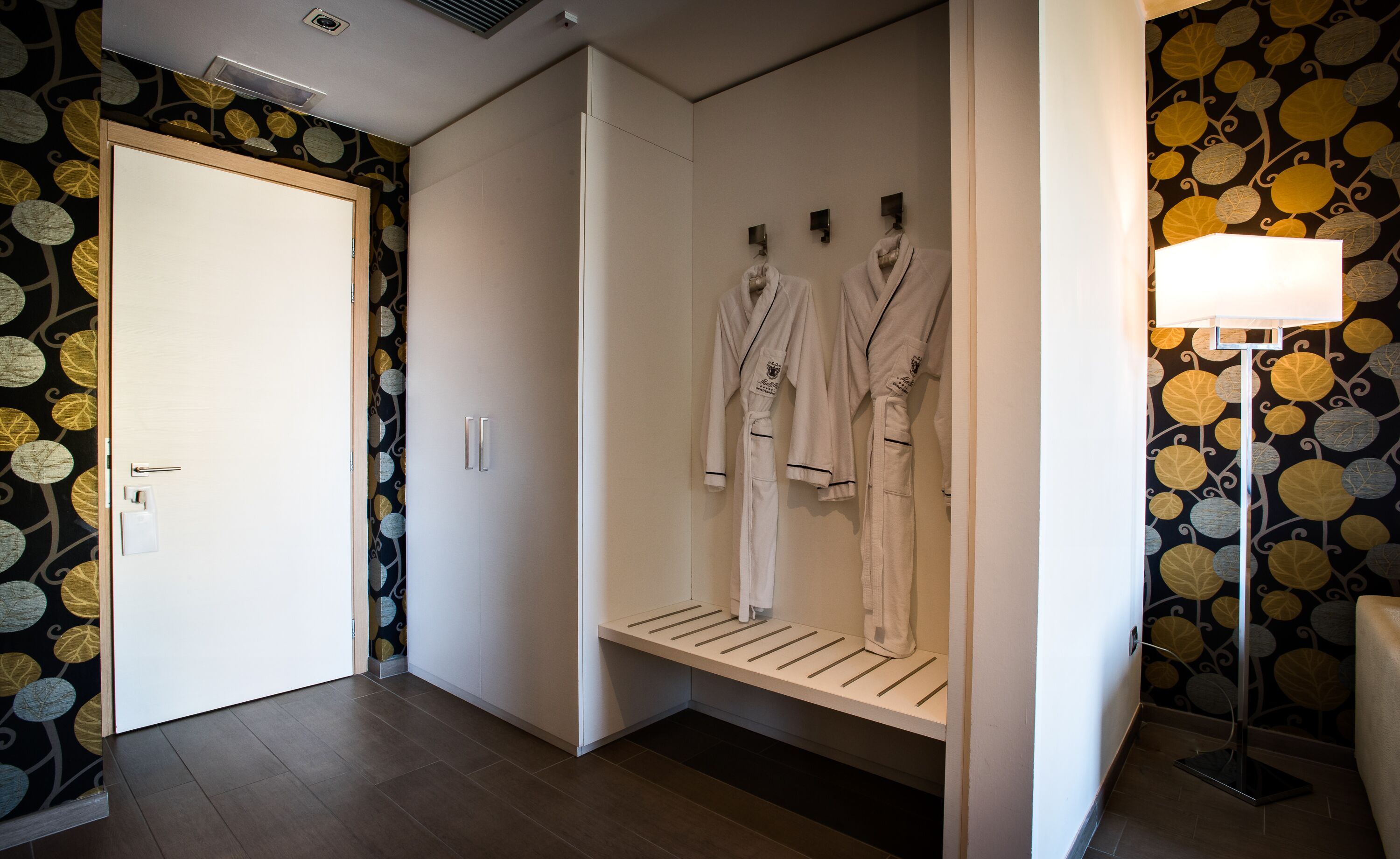 Ein Hotelzimmer mit Kleiderschrank, einer Bank mit Bademänteln und einer Wand mit Muster.