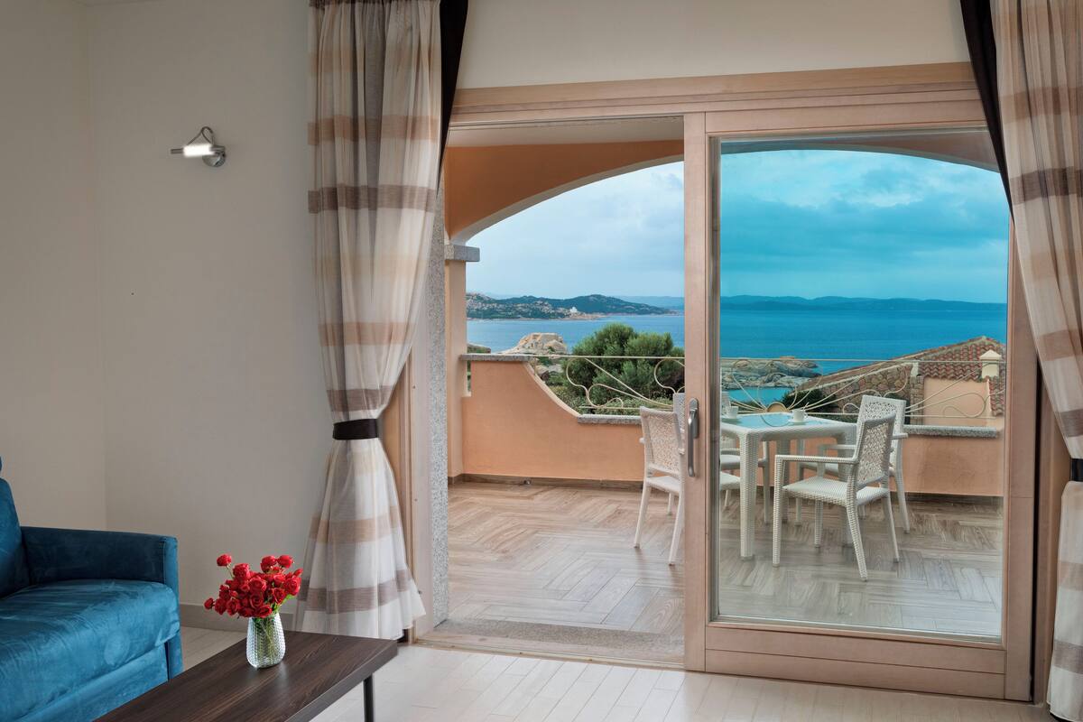 A balcony with a view of the sea, a table with chairs, and a blue sofa.
