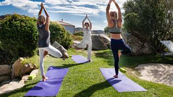 Three individuals practicing yoga on outdoor mats in a grassy area with rocks and trees.