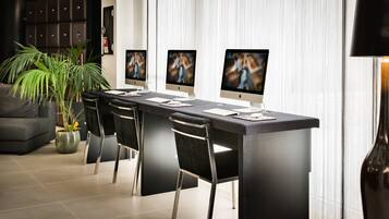 A modern reception desk with three monitors, black chairs, and a potted plant.