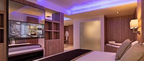 A modern hotel room with a large bed, a mirror, and a television displaying the hotel's amenities.