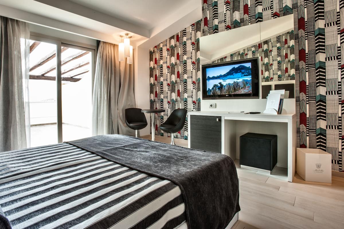 A hotel room with a bed, a desk, a television, and patterned wallpaper.