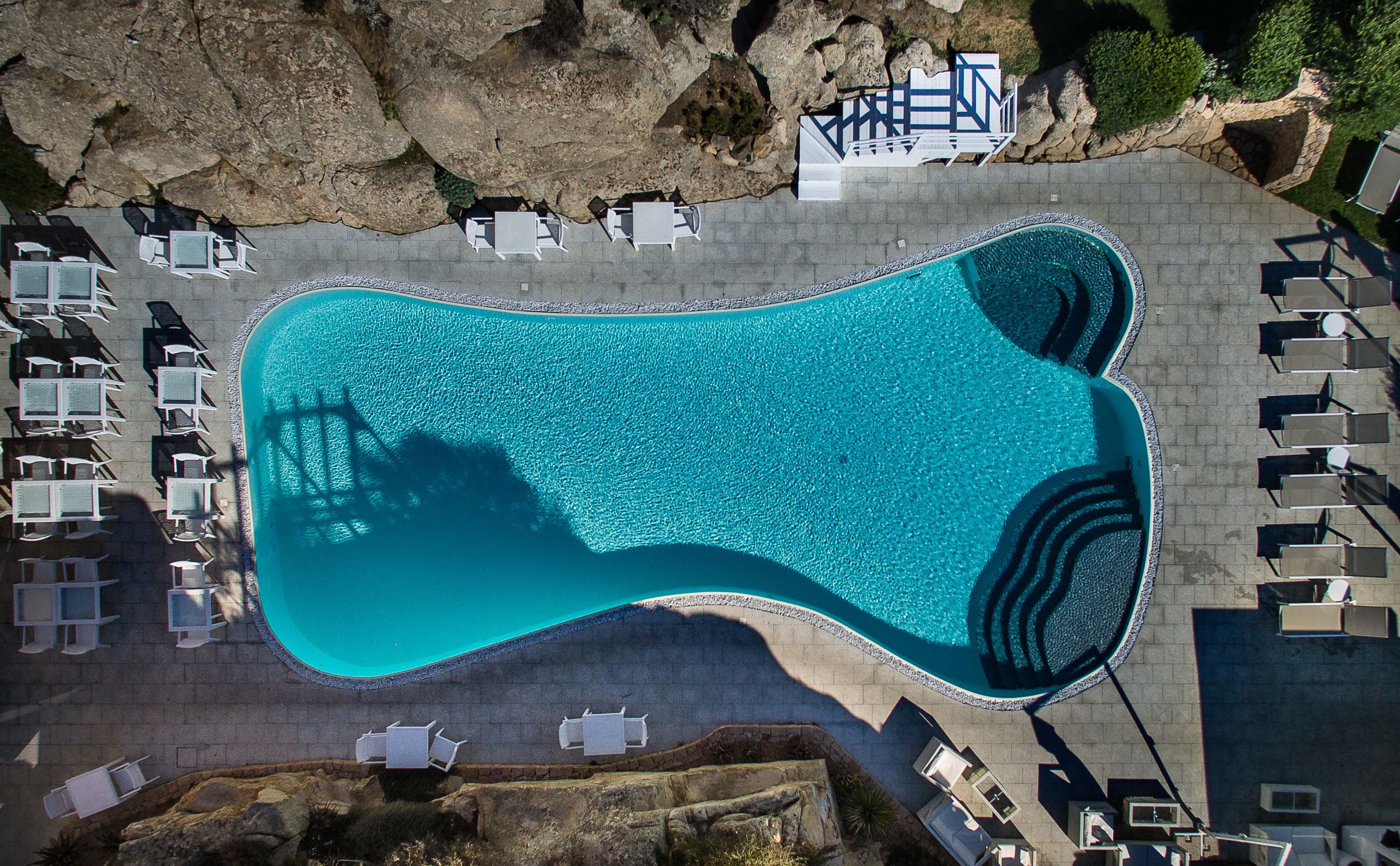 Vista aèria d'una piscina envoltada de gandules i una paret de pedra.