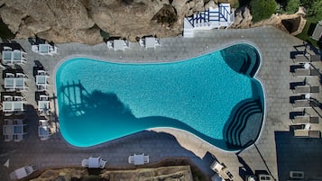 Vista aèria d'una piscina envoltada de gandules i una paret de pedra.