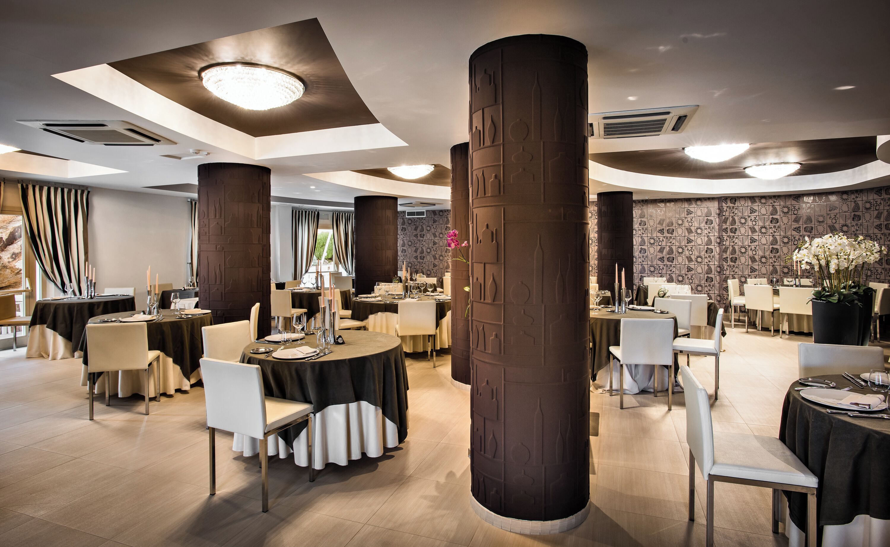 Un comedor amplio con varias mesas redondas, techos altos y columnas decorativas.