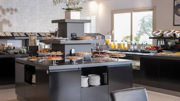 Una barra de desayuno moderna con una variedad de pasteles y bebidas, una estación de café y vistas al exterior a través de grandes ventanales.