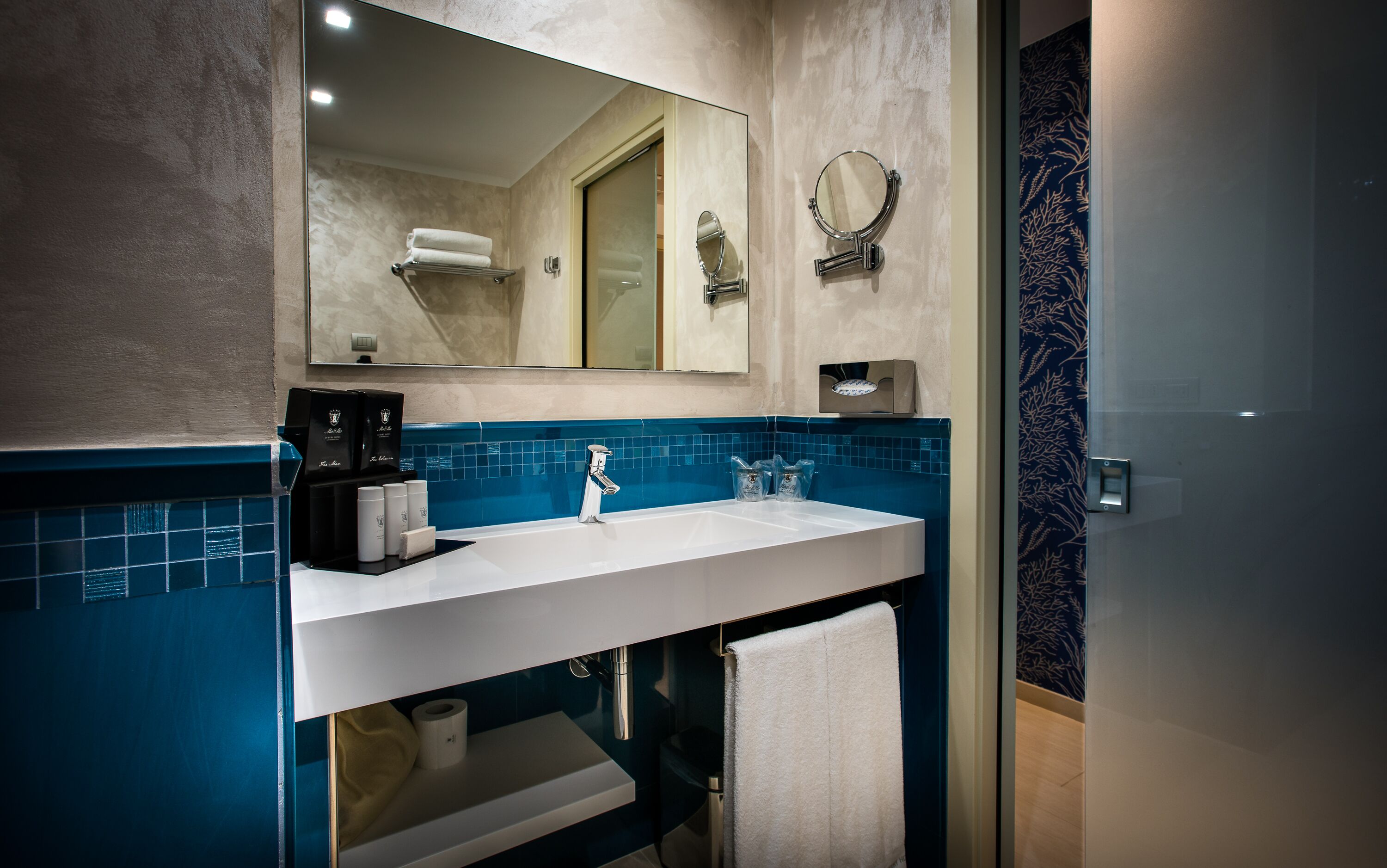 Een moderne badkamer met een witte wastafel, een blauw betegelde spatwand en een grote spiegel.