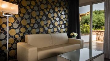 A modern living room with a beige sofa, a glass coffee table, and a patterned wallpaper.