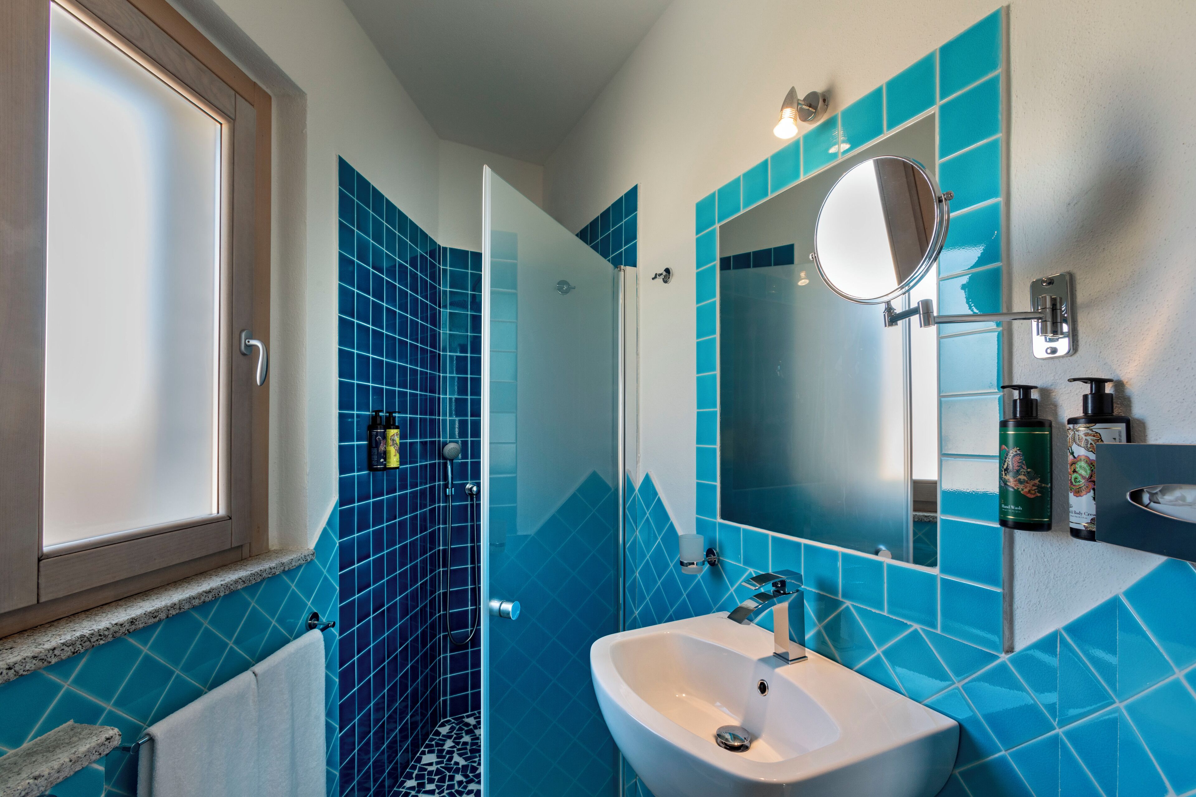 Un baño con lavamanos, espejo y paredes de azulejos azules.
