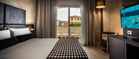 A hotel room with a large bed, a small table, a TV, and a balcony with curtains.