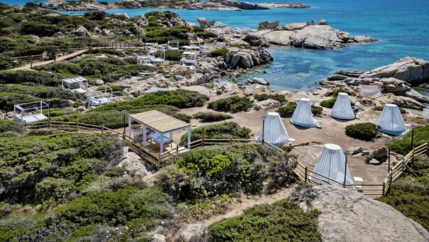 Um resort costeiro com várias tendas brancas, uma estrutura de madeira e terreno rochoso.