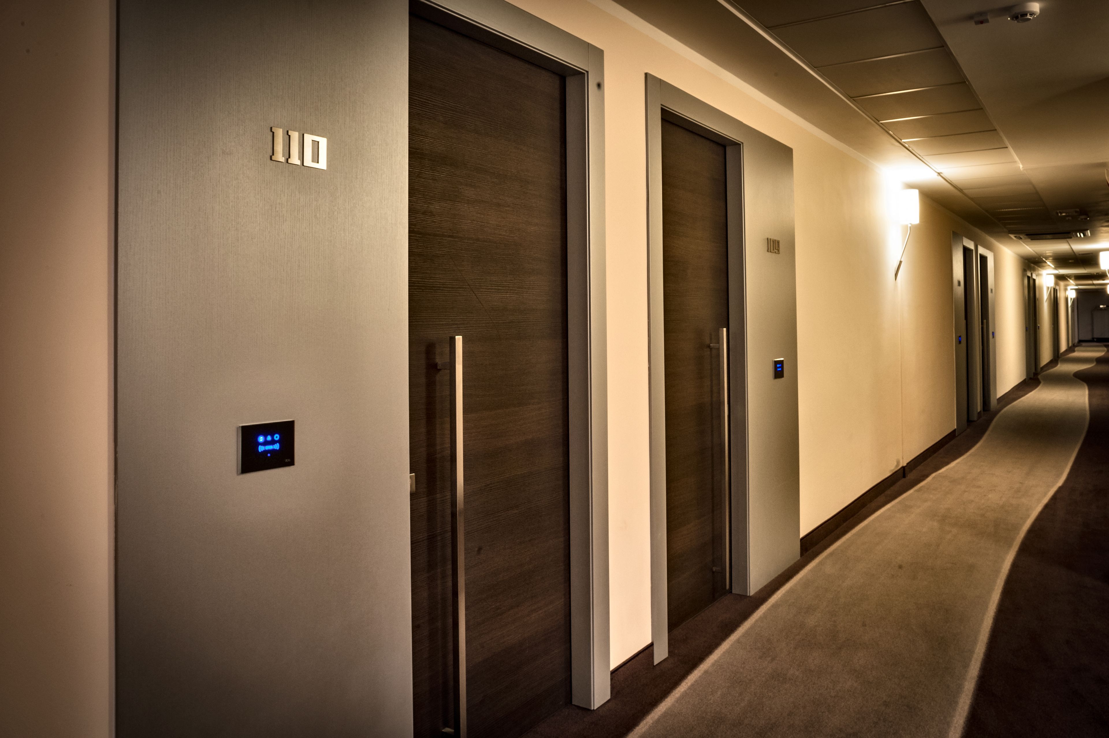 A hotel corridor with doors, a digital display, and a carpeted floor.