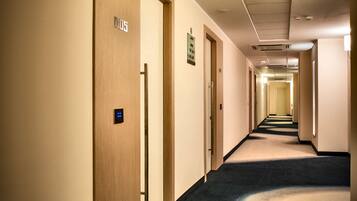 A long, narrow hotel corridor with wooden doors, a carpeted floor, and a ceiling with recessed lighting.