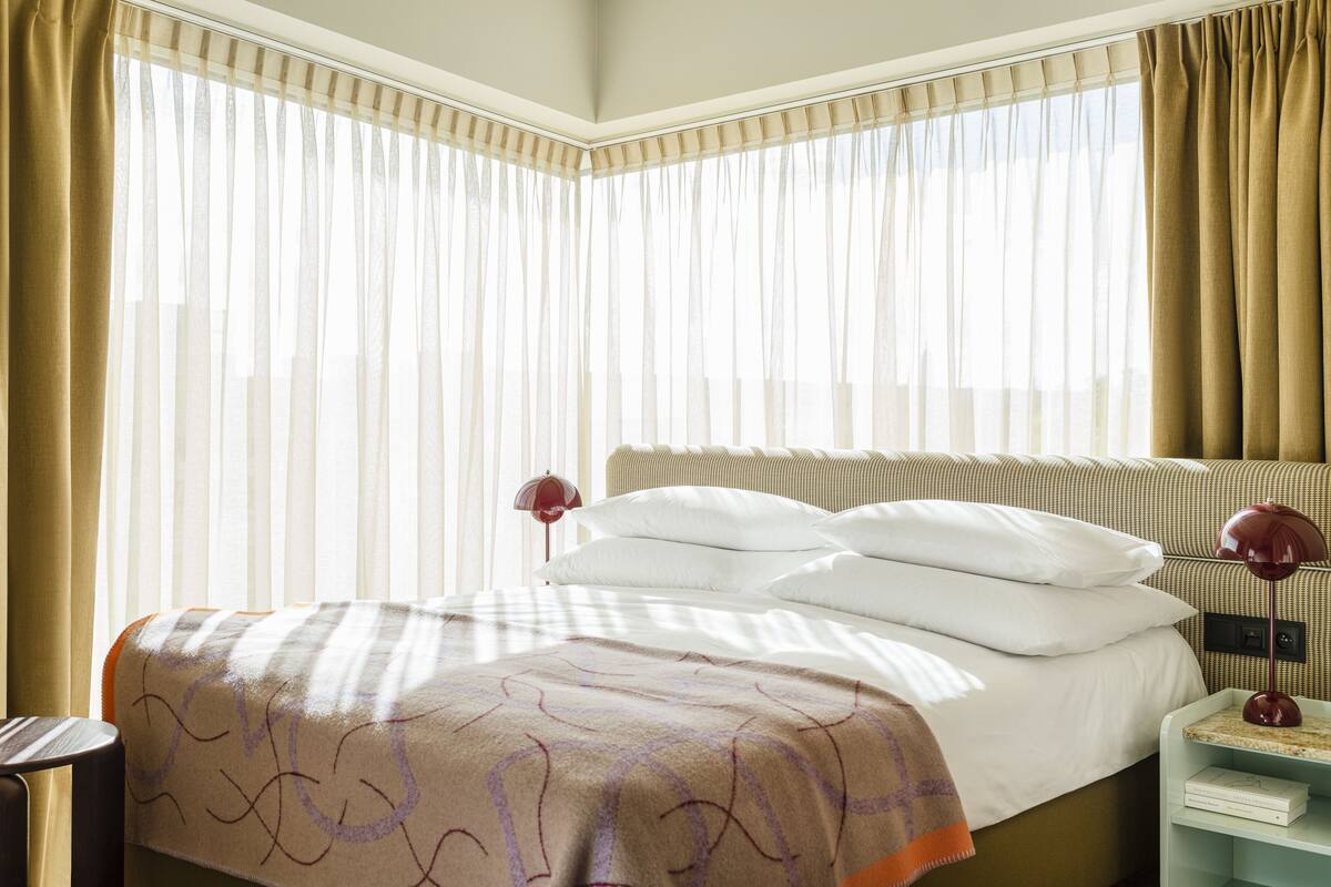 Een net opgemaakt bed met een geborduurd kleed, een bedlampje en een nachtkastje met een boek.