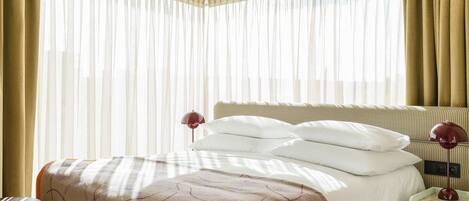 A neatly made bed with a patterned blanket, a bedside lamp, and a nightstand with a book.