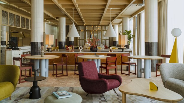 A spacious hotel lobby with high ceilings, large windows, and a central seating area with multiple tables and chairs.