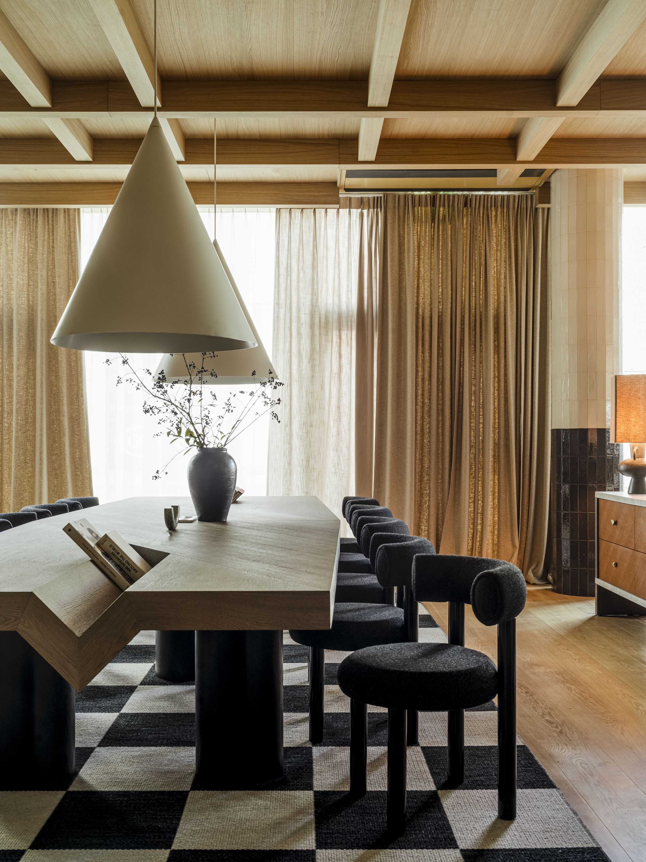 A modern dining area with a wooden table, black and white checkered rug, and a hanging light fixture.