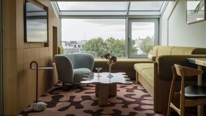 A modern living room with a large window, a sofa, a chair, and a coffee table with a vase.