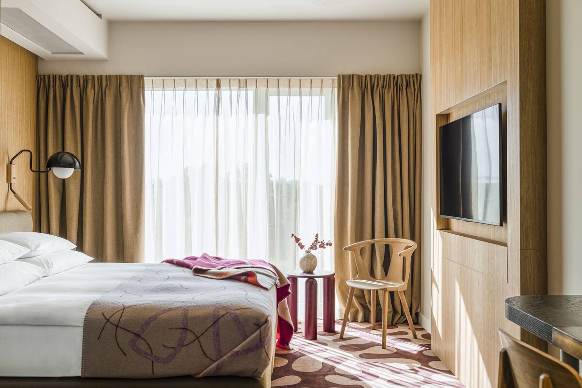 Een hotelkamer met een bed, een aan de muur bevestigde televisie, een tafeltje met een vaas en een stoel.