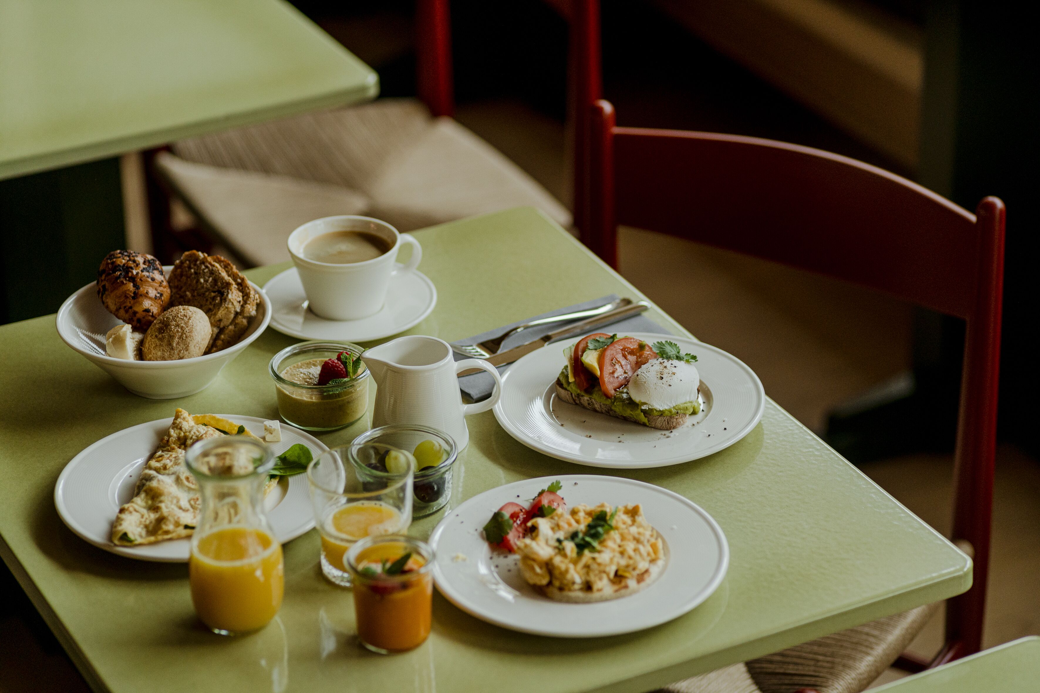 A breakfast table with various dishes, including toast, eggs, and pastries, along with cups of coffee and juice.