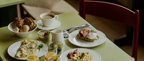 A breakfast table with various dishes, including toast, eggs, and pastries, along with cups of coffee and juice.
