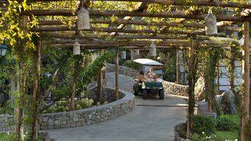 A pathway with a stone wall on one side and a wooden pergola with hanging lanterns.