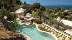 A pool area with a view of the sea, surrounded by greenery and stone structures. - Botania Relais & Spa - The Leading Hotels of the World. (Forio)