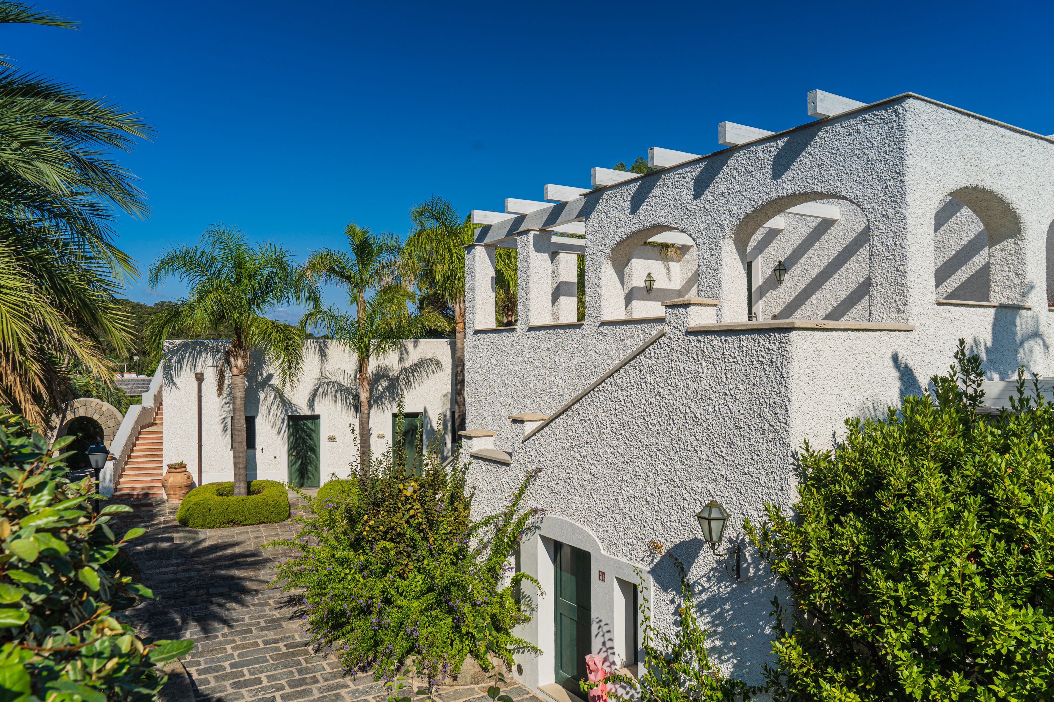 A white building with arched windows and a stone staircase leading to a door.