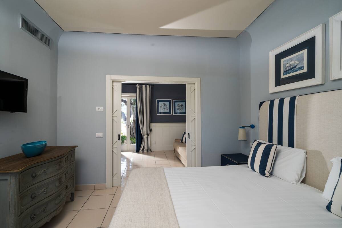 A bedroom with a bed, a dresser, a nightstand, and a wall-mounted TV.