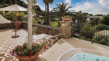 Un patio con jacuzzi, mobiliario exterior y una pared de piedra.