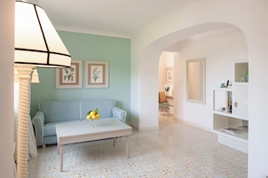 Una sala de estar con un sofá, una mesa de centro y una lámpara. En la pared hay cuadros enmarcados y una estantería con libros y objetos decorativos.