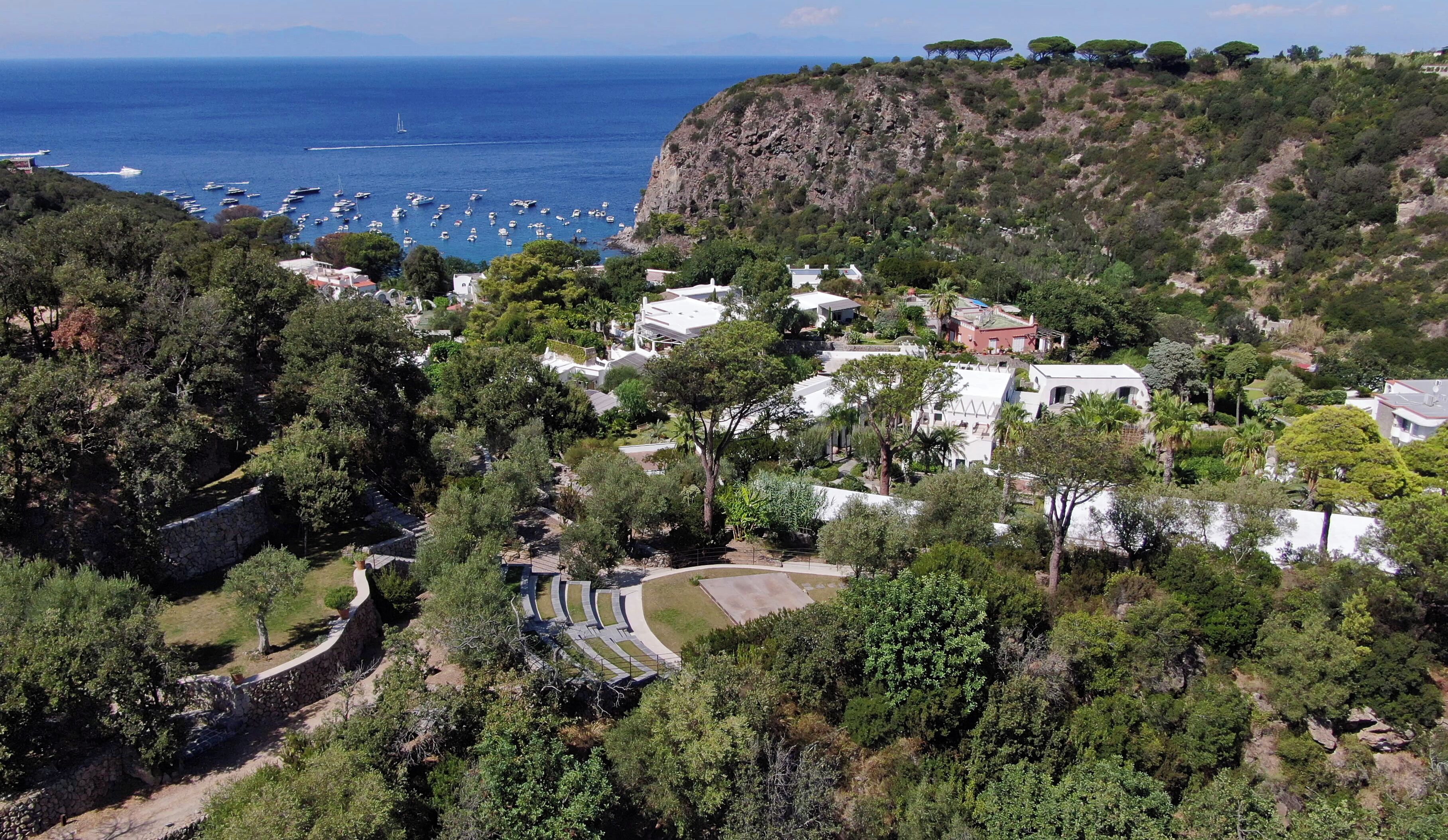 Un borgo costiero con case circondate da vegetazione lussureggiante e una scogliera rocciosa.