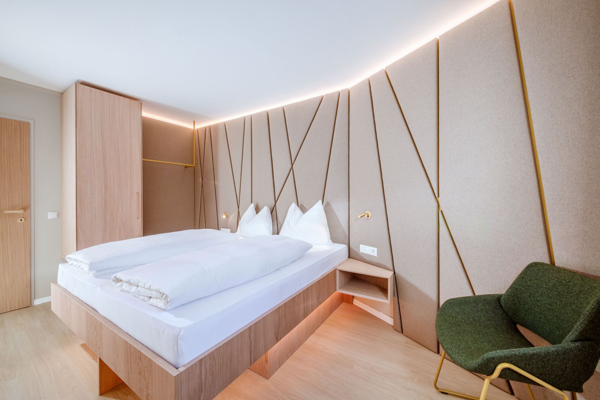A modern bedroom with a wooden bed, a green chair, and a unique wall design.
