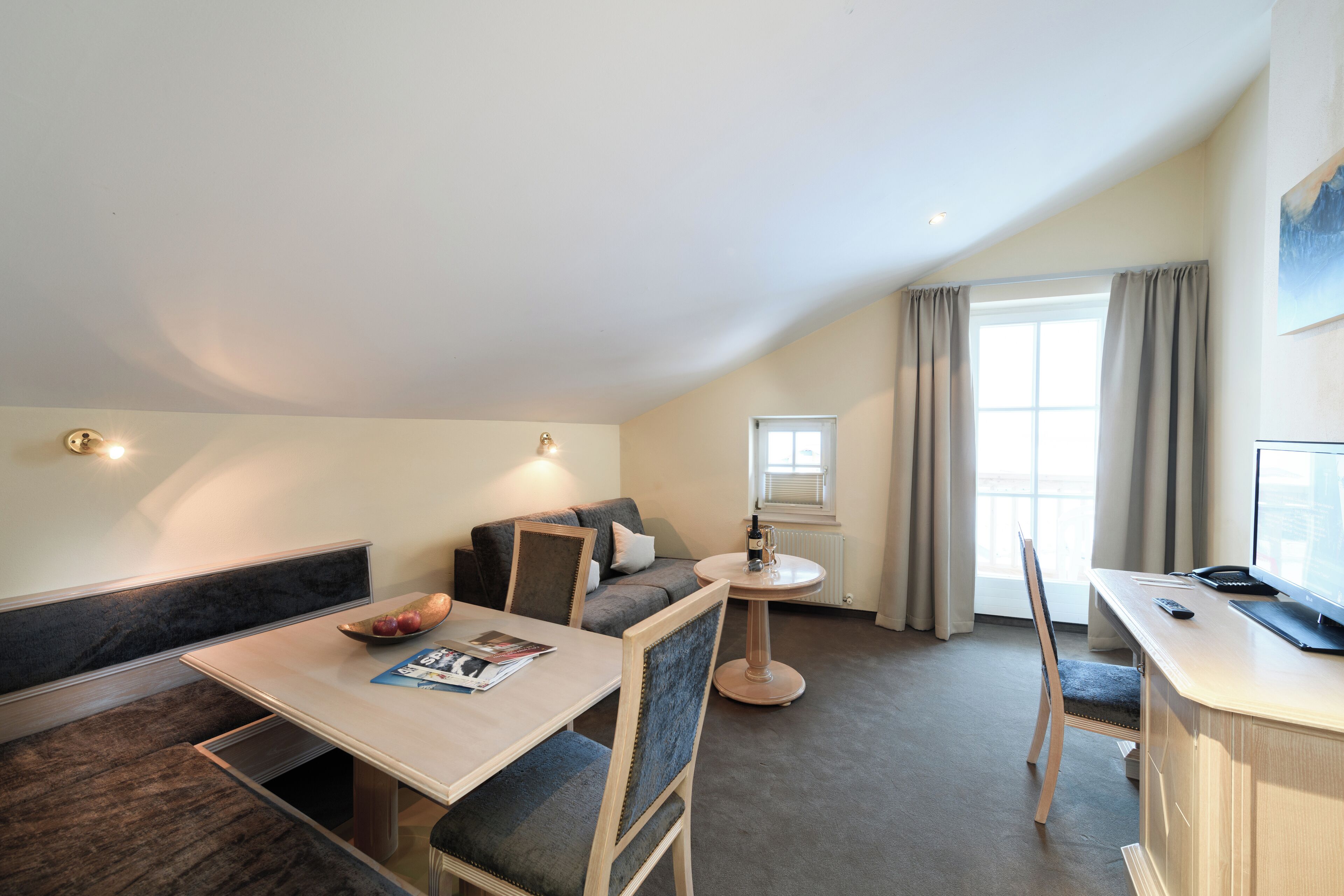 Une chambre d’hôtel moderne comprenant un coin repas, un canapé, une petite table ronde et un bureau avec un ordinateur.