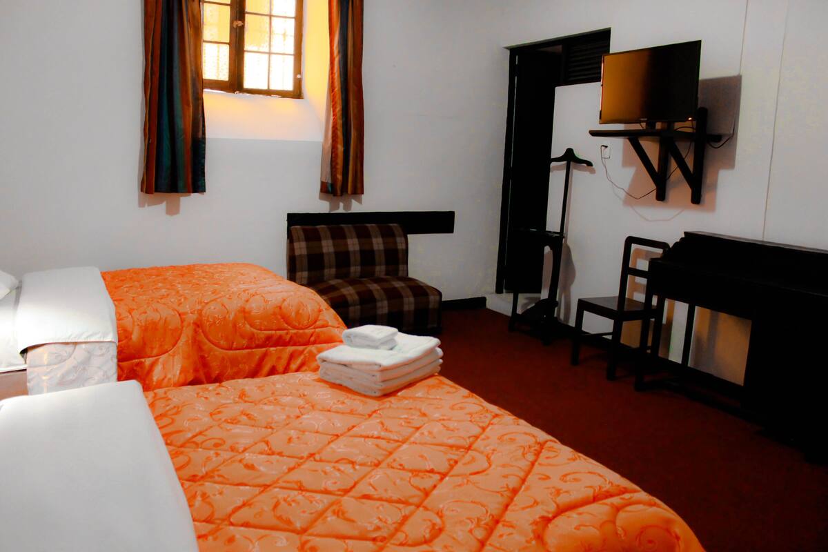 Habitación de hotel con dos camas, un escritorio, una silla y un televisor.
