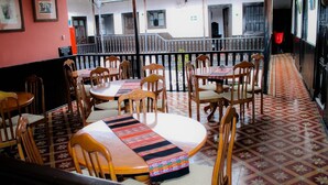A dining area with round tables and wooden chairs, a patterned floor, and a balcony with a railing. - Hotel Casablanca (Cajamarca)