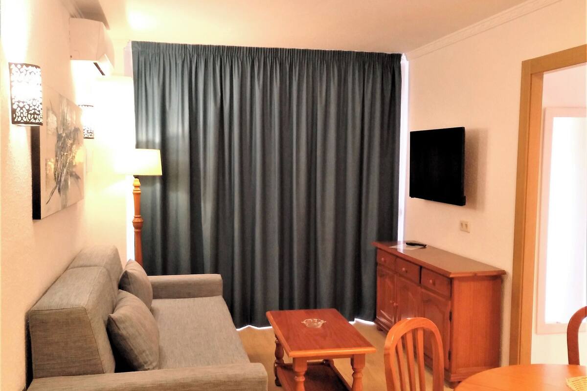 Uma sala de estar com sofá, mesa de madeira e televisão na parede.