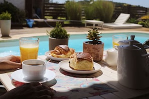 Desayuno junto a una piscina, con una taza de café, dos pasteles, un vaso de zumo de naranja y una tetera.