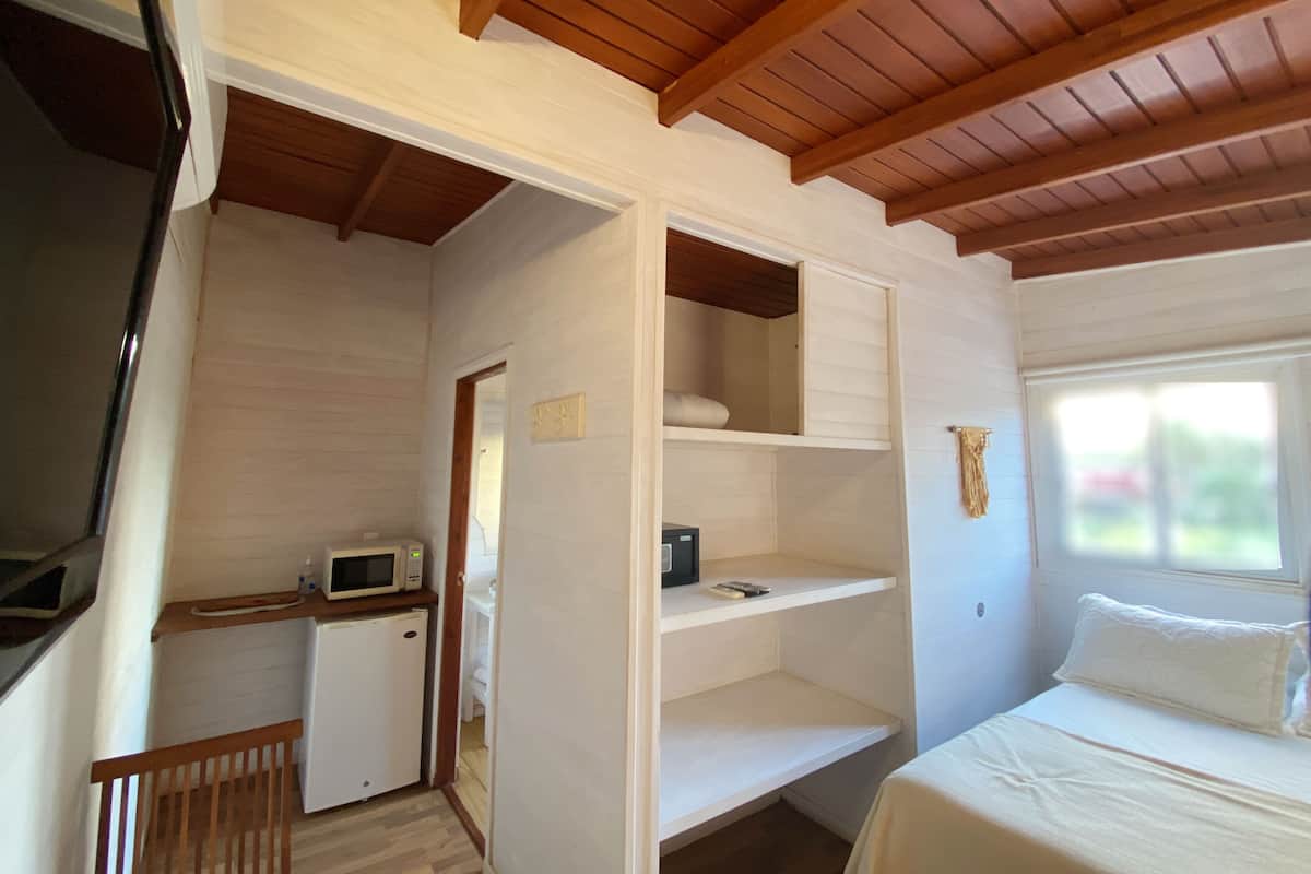 A bedroom with a bed, a small kitchenette, and a wooden ceiling.