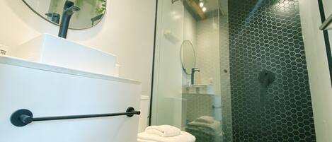 A bathroom with a white toilet, a glass-enclosed shower with a honeycomb pattern, and a round mirror on the wall.