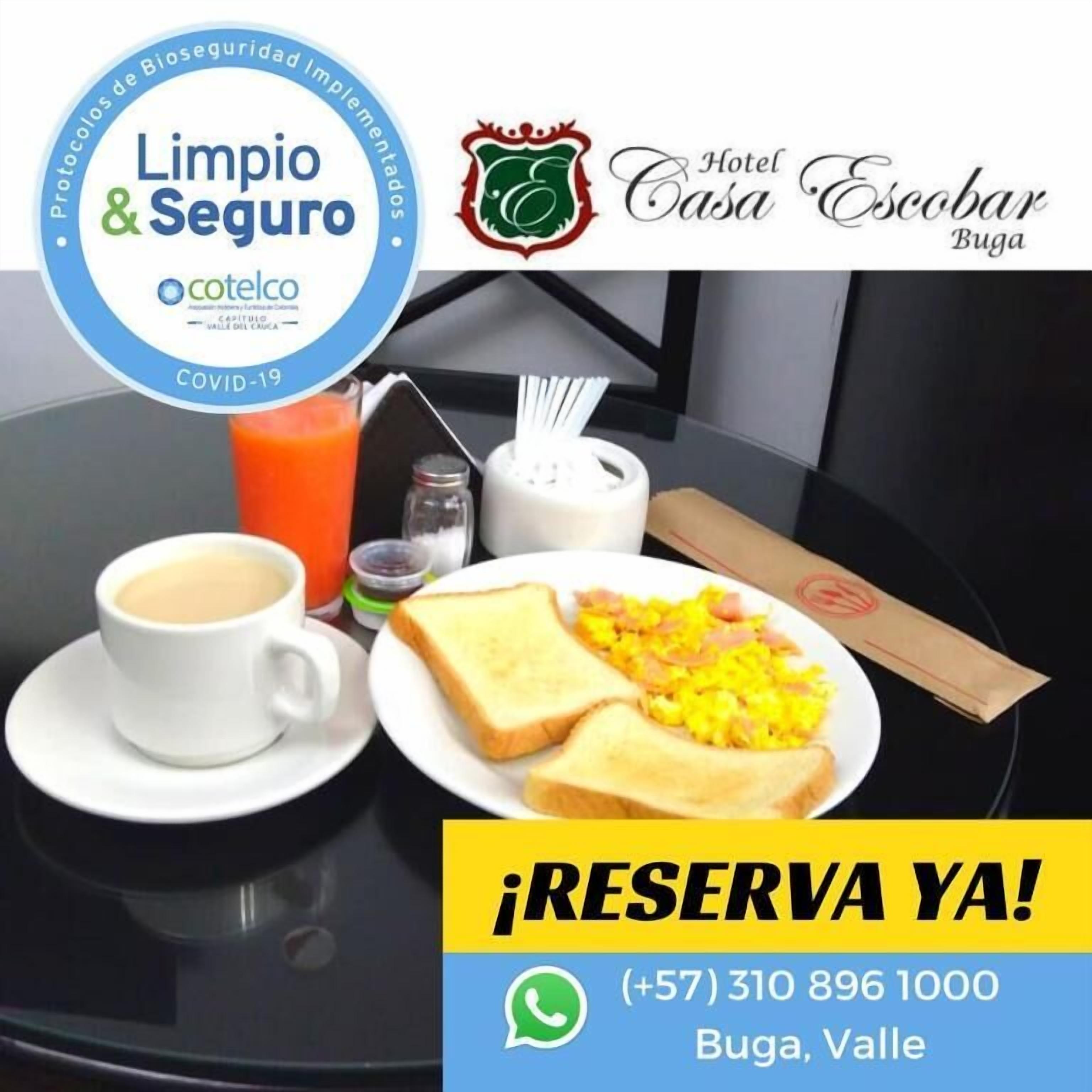 Un desayuno con una taza de café, tostadas, huevos revueltos y un vaso de jugo de naranja sobre una mesa. También hay saleros y pimenteros, una servilleta y un menú. La imagen incluye los logotipos de 'Hotel Casa Escobar Buga' y 'Limpio & Seguro'.