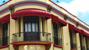 Un edificio con fachada curva, balcones con barandas de metal y un letrero que indica un restaurante llamado “Pollo Asado”.