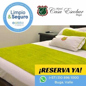 A hotel room with a bed, pillows, and a nightstand. There is a logo for 'Hotel Casa Escobar Buga' and a '¡RESERVA YA!' sign with a phone number. - Hotel Casa Escobar Buga (Guadalajara de Buga)