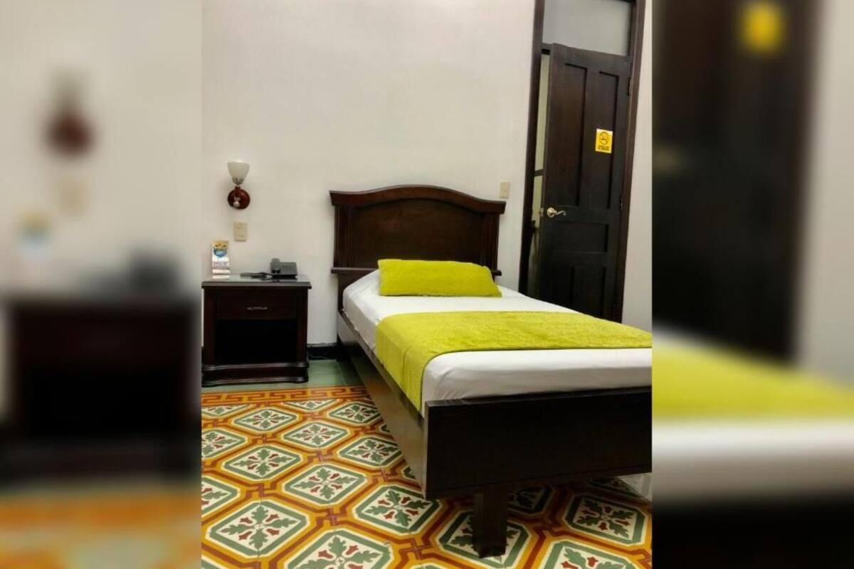 A room with a bed, a nightstand, a lamp, and a patterned floor.