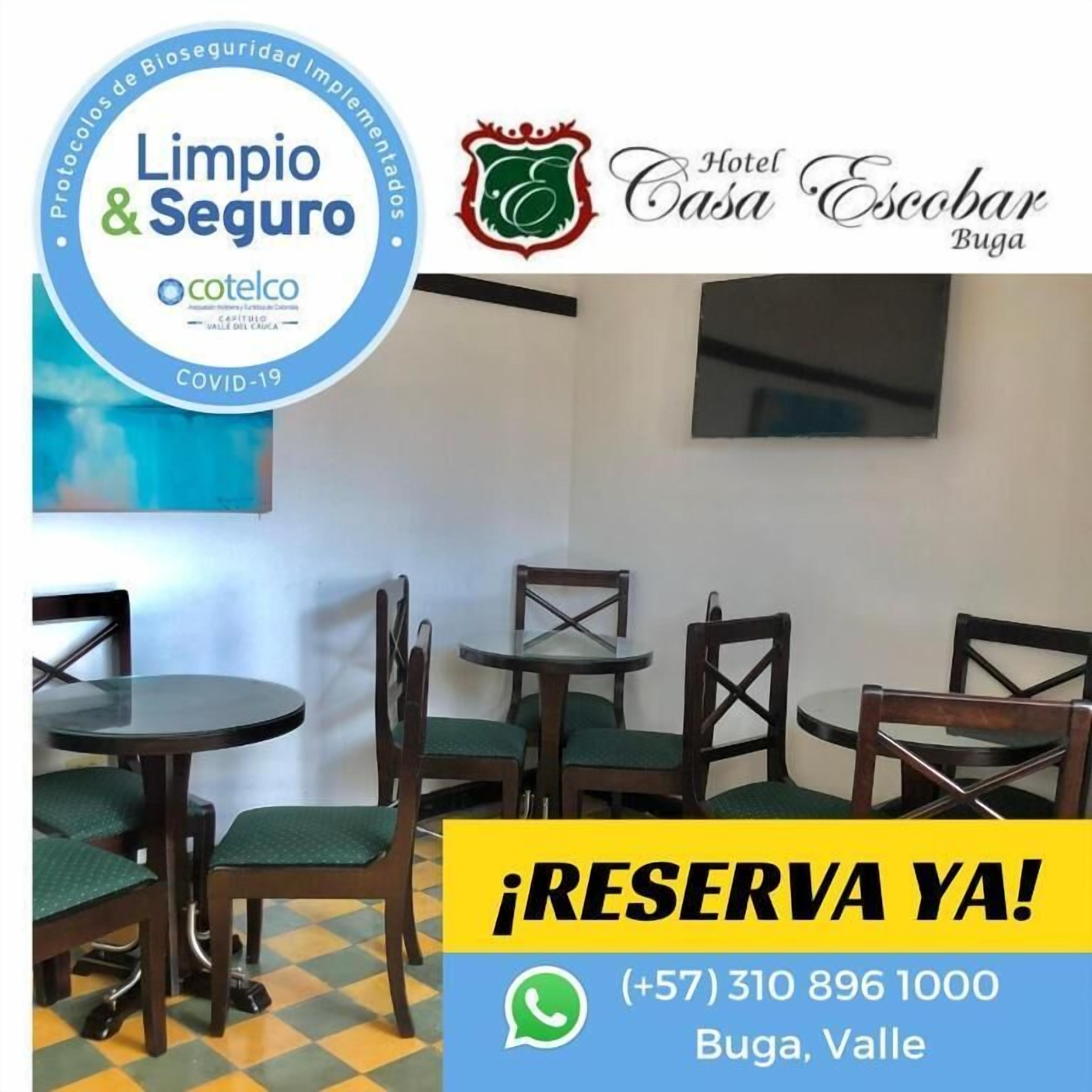 Habitación de hotel con comedor que incluye sillas y mesas de madera, un televisor de pantalla plana en la pared y un letrero de recepción.