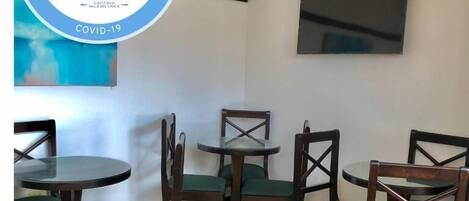 Habitación de hotel con comedor que incluye sillas y mesas de madera, un televisor de pantalla plana en la pared y un letrero de recepción.